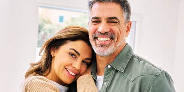 A close-up portrait of a happy, affectionate mature man and woman hugging at home and looking at the camera; illustrating 'the relational anchoring model' where classic commitment patterns survive generational shifts.