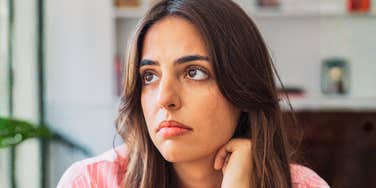 A close-up portrait of an anxious woman in deep thought, looking off-camera against a neutral backdrop; illustrating 'the institutional threat assessment model' where public safety concerns necessitate heightened individual vigilance.