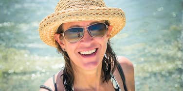 A happy 50-year-old woman smiling and enjoying life on a sunny beach; a visual representation of 'the unplugged vitality' that defines the self-reliant Gen-X generation.