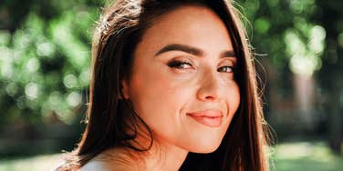 An outdoor portrait of a young woman enjoying a sunny park stroll, representing emotional safety, genuine rapport, and low-stress communication.