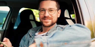 A close-up portrait of a young man holding a cellphone in a car interior, illustrating casual communication, low relationship readiness, and digital dating habits.