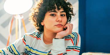 A pensive woman resting her chin on her hand, displaying a thoughtful expression, emotional composure, and relaxed social presence.
