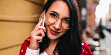 An outdoor photograph of a woman with red lipstick laughing while on a phone call, illustrating low-stress social connection, self-assurance, and high emotional regulation.