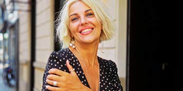 Woman smiling outdoors in an urban setting with short blonde hair and a patterned dress, showing confidence and happiness on a sunny day in the city street exterior