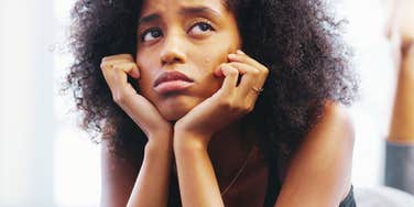 A pensive Black woman sitting alone in a quiet bedroom, illustrating the psychological impact of chronic rumination, emotional burnout, and lingering regret.