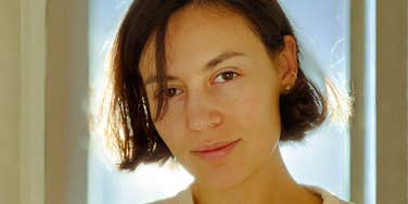 A backlit woman looking directly into the camera with an intense yet calm expression, bathed in soft golden rim light that conveys deep intimacy, clarity, and unforced emotional presence.