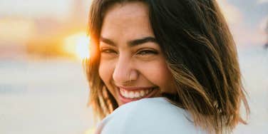 A woman looking over her shoulder with a warm, genuine smile during a golden hour sunset, capturing effortless joy, ease, and intimate companionship.