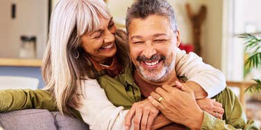 An older multiethnic couple sharing a lighthearted laugh while hugging at home, illustrating emotional resonance, lifelong intimacy, and relational attunement.