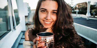 A close-up photograph of a woman smiling radiantly while enjoying a warm beverage, illustrating emotional wellbeing, security, and peaceful partnership.