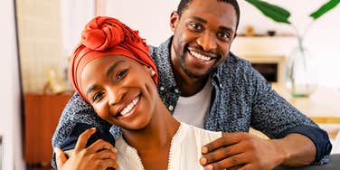 A relaxed couple smiling and holding each other in a cozy living room, illustrating relational stability, micro-connections, and long-term attachment.