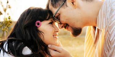 An intimate outdoor photograph of a man and woman resting their foreheads together in golden light, illustrating high emotional safety, secure attachment, and relational warmth.