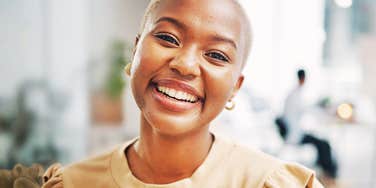 Close-up corporate portrait of a confident Black female entrepreneur smiling warmly in a bright modern workspace, radiating emotional stability and mental strength