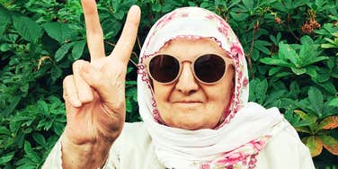 A close-up outdoor portrait of a smiling older woman with grey hair wearing modern sunglasses; illustrating 'the functional agency matrix' where late-life independence thrives.