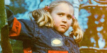 Vintage early eighties style snapshot of a solitary young girl looking directly toward the camera with a guarded, careful expression; illustrating 'the intergenerational conditioning framework' where children learn to suppress personal needs.