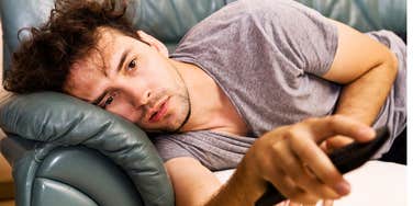 A middle-aged man lying on a couch with a remote in hand, exemplifying passive screen time, burnout, and low-motivation daily habits.