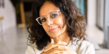 A confident middle-aged hispanic woman poses in a well-lit office interior, exuding professionalism and experience.