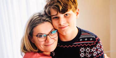 A happy mother warmly hugging her smiling teenage son indoors; a visual representation of 'the secure collaborator' archetype found in alternative education and homeschooling lifestyles.