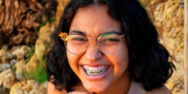 A close-up photograph of a happy teenage girl with glasses giggling naturally, illustrating the positive psychological impact of relaxed, supportive parenting.