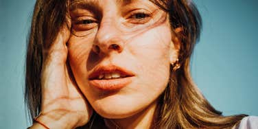 Outdoor portrait of a curly-haired woman hand on cheek with a slightly flustered and embarrassed glance, illustrating the emotional toll of dealing with casual gender microaggressions.