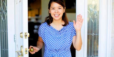 waving happy woman opening front door for guests