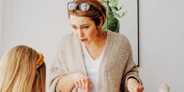 A stressed woman scolding her young daughter for bad behavior in a home setting; a visual representation of 'the disciplinary friction' that marks the most stressful phase of childhood.