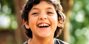 A young boy smiling happily in nature with bright sunlight, symbolizing joyful childhood, emotional health, and positive parenting.