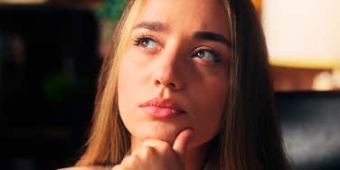 A close-up portrait of a thoughtful young woman resting her chin on her hand in deep reflection, symbolizing self-awareness, active listening, and high emotional intelligence.