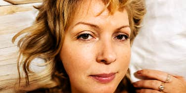 A mature woman relaxing on pillow looking thoughtfully into the camera, symbolizing positive aging, inner peace, and generational wisdom.