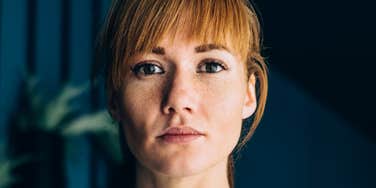 A low-angle portrait of a confident, elegant woman looking seriously into the camera while standing in a modern home environment.