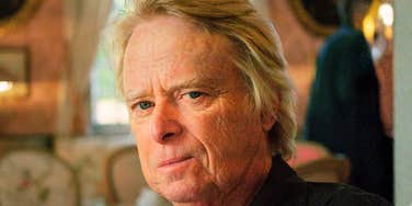 A close-up portrait of an older Baby Boomer man giving an unsatisfied, skeptical grin directly at the camera.