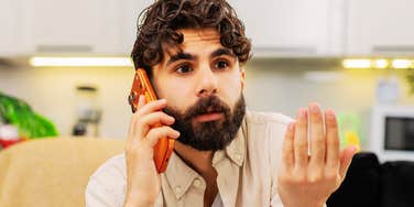 An annoyed man gesturing with his hand while making a phone call indoors, symbolizing marital tension, communication breakdown, and loss of respect.