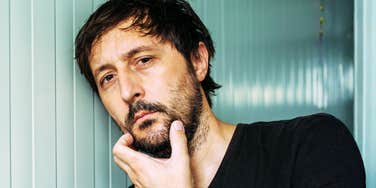 A close-up studio shot of a thoughtful man resting his chin on his hand, symbolizing deep evaluation, emotional guarding, and strategic ambiguity.