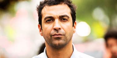 A serious portrait of a man looking directly into the camera with an unreadable, intense, and guarded expression.