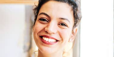 A confident young woman smiling broadly indoors, symbolizing executive presence, approachable authority, and workplace leadership.