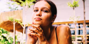 A close-up portrait of a thoughtful woman sitting at a street cafe terrace resting her chin on her hand and looking off into the distance.