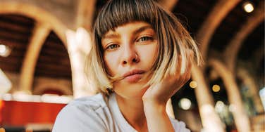 A close-up portrait of an attractive European woman with short hair looking directly into the camera with an unimpressed, bored expression.