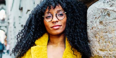 A woman with curly hair and round glasses looking directly into the camera with a calm, self-assured expression, symbolizing self-awareness, emotional grounding, and personal growth.
