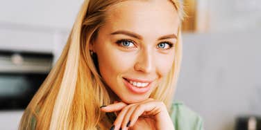 A smiling blonde woman looking forward in a modern room, symbolizing emotional intelligence, effective workplace communication, and assertive self-awareness.