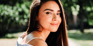 A young woman looking back with a warm and gentle smile outdoors, symbolizing charisma, social intelligence, and natural human connection.