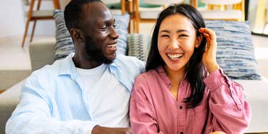 A close-up lifestyle shot of a happy couple laughing together in the sunlight, representing mutual emotional openness, warmth, and relationship satisfaction.