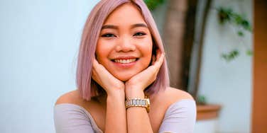 young Gen Z woman smiling with her hands on her chin