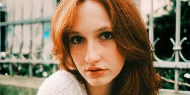 A red-haired woman in a white blouse posing calmly outdoors, symbolizing emotional regulation, self-respect, and clear communication boundaries.