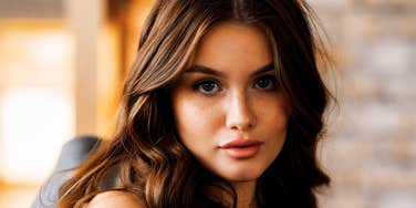 A young woman with long wavy hair looking straight into the lens indoors, symbolizing poise, personal boundaries, and effortless respect.