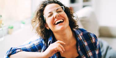 A woman relaxing on a sofa and laughing warmly, symbolizing emotional availability, natural charm, and romantic magnetics.