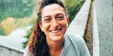 A joyful woman with curly hair smiling outdoors near a scenic road, symbolizing freedom, accessible leisure, and financial peace.