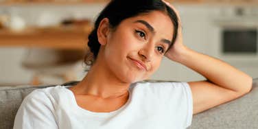 A portrait of a confident woman sitting comfortably on a couch, looking relaxed and composed in a home environment.