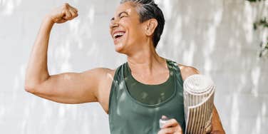 Woman who is mentally and emotionally strong flexes happily with her yoga mat