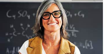 A happy female high school science teacher standing confidently in front of her students, representing positive classroom culture and smooth instructional flow.