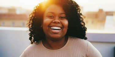 A young woman laughing happily on a rooftop terrace during golden hour, symbolizing independence, modern freedom, and generational shifts.