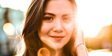 A beautiful young woman looking at the camera with a gentle, confident expression in golden hour sunlight, symbolizing self-respect, romantic charisma, and emotional integrity.